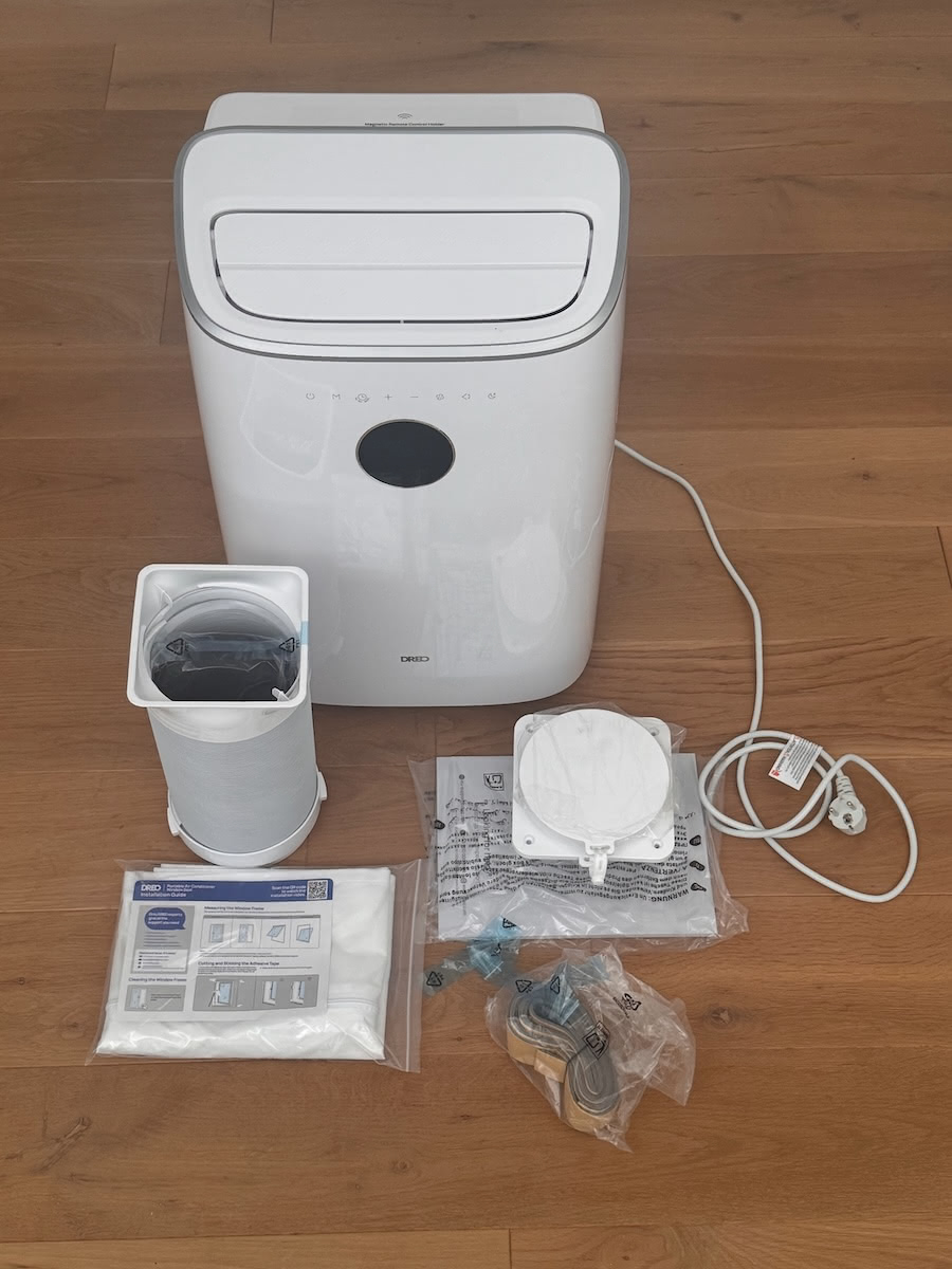 Lieferumfang der Dreo Mobile Klimaanlage 318S: Gerät, Abluftschlauch, Fensterblenden, Wandadapter, Dichtungsmaterial und Netzkabel auf dem Boden ausgelegt