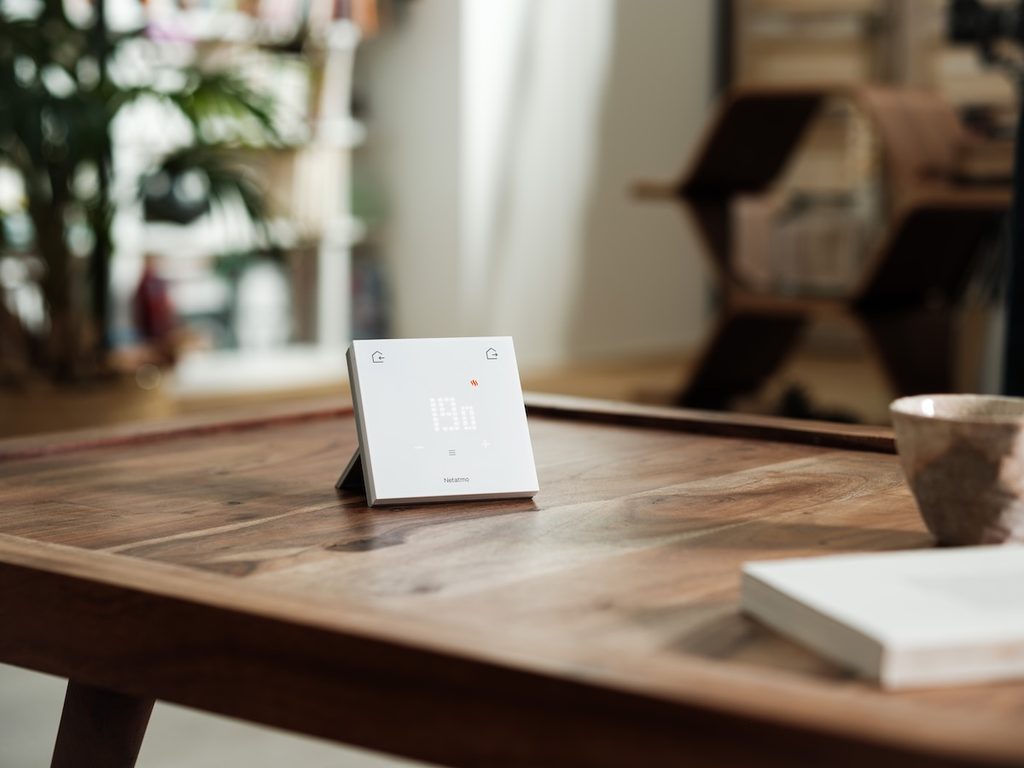 Netatmo Smartes Thermostat Original mit Display auf einem Holztisch, daneben eine Tasse und ein Buch