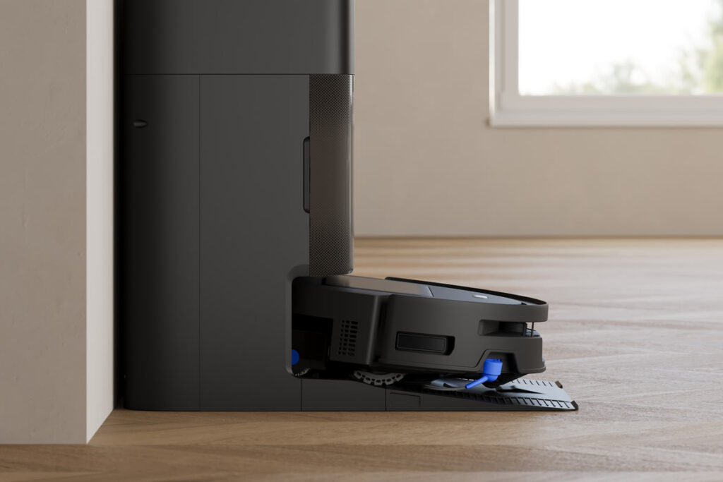 Ecovacs Deebot T90 Max Pro Omni fährt in seine schwarze Ladestation, im Hintergrund ein Fenster mit Blick ins Grüne.