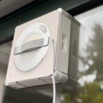 Ecovacs Winbot W2S Omni im Test: Der Fensterputzroboter haftet an einer Fensterscheibe, dahinter Bäume im Garten