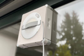 Ecovacs Winbot W2S Omni im Test: Der Fensterputzroboter haftet an einer Fensterscheibe, dahinter Bäume im Garten