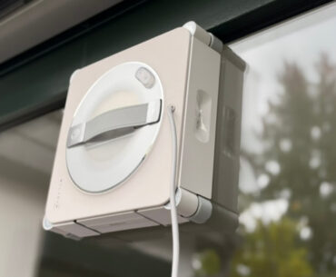 Ecovacs Winbot W2S Omni im Test: Der Fensterputzroboter haftet an einer Fensterscheibe, dahinter Bäume im Garten