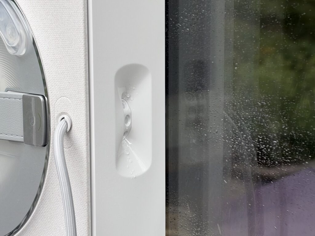 Nahaufnahme: Der Ecovacs Winbot W2S Omni sprüht Reinigungslösung als feinen Nebel auf die Fensterscheibe